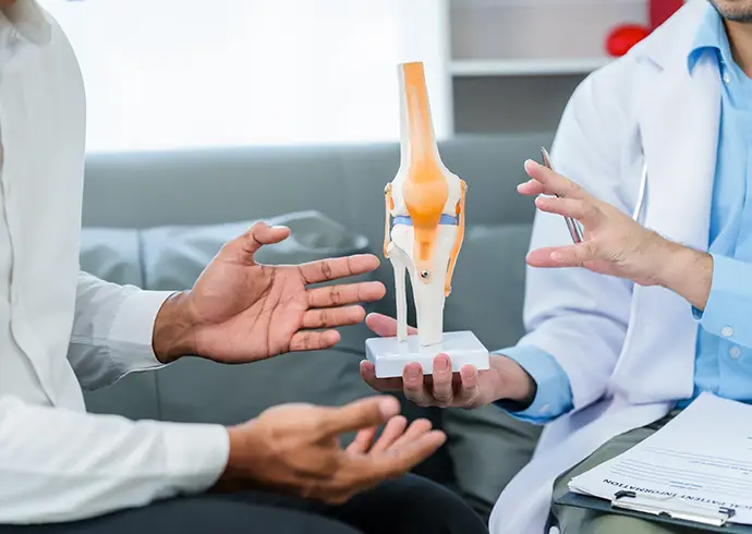 male patient and male doctor discussing a model of a knee joint, likely focusing on condition of knee arthritis during a medical consultation