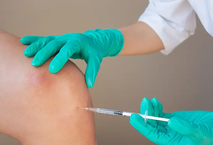 doctor in green gloves gives a young man an intra-articular injection of hyaluronic acid against osteoarthritis in the knee joint